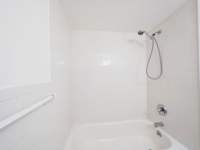 white tub/shower combo in bright bathroom, detachable shower head, towel rack