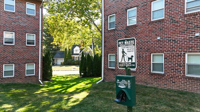 pet friendly apartments, pet waste basket with bags in green grassy area between two brick buildings
