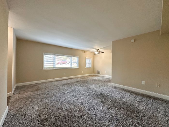 spacious carpeted living room, ceiling fan, large windows