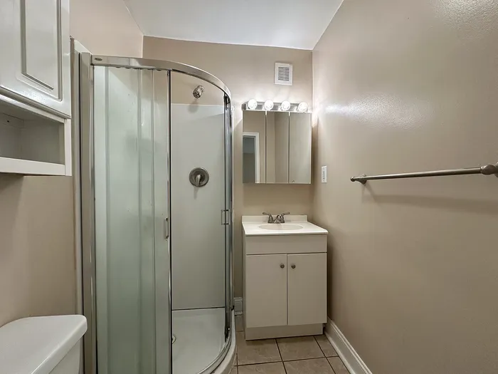 renovated bathroom with tile floor, corner shower with sliding door, medicine cabinet, storage shelfs, vanity sink