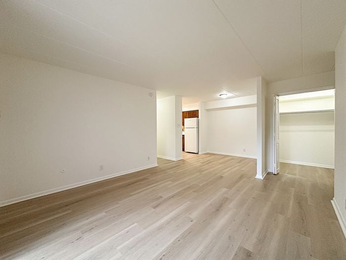 Bright and airy open-plan apartment featuring elegant wooden flooring, a spacious living area, and a convenient kitchen with a large refrigerator.
