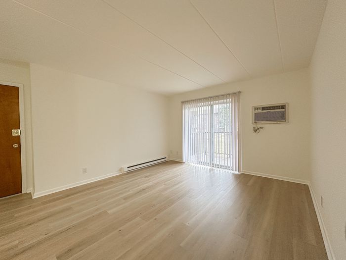 Bright, open-plan living area with modern laminate flooring and large sliding glass doors leading to a serene outdoor view.