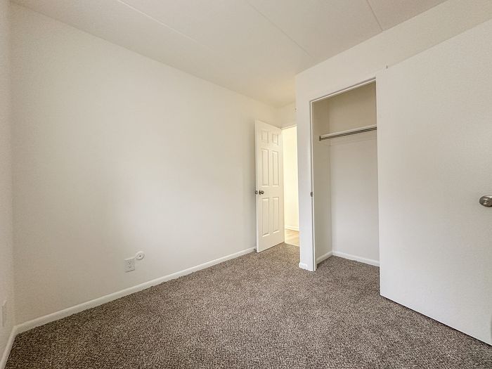 Bright and airy bedroom with soft carpet flooring and a spacious closet, perfect for personalized decor.