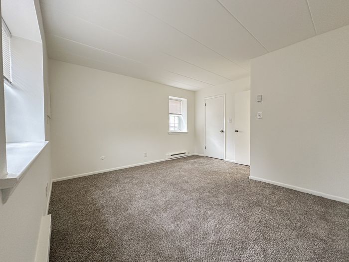 Spacious, sunlit room with a cozy carpeted floor and modern white walls, ideal for comfortable living.