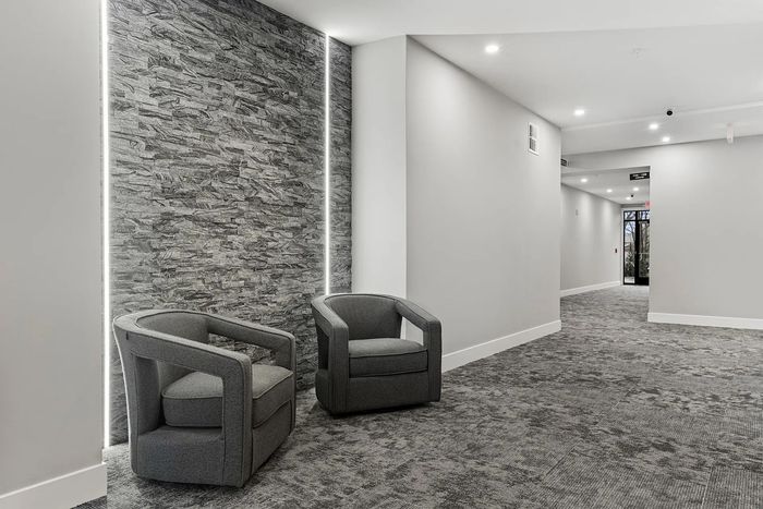 Contemporary apartment hallway with sleek gray chairs and modern stone accent wall, offering a sophisticated entrance.