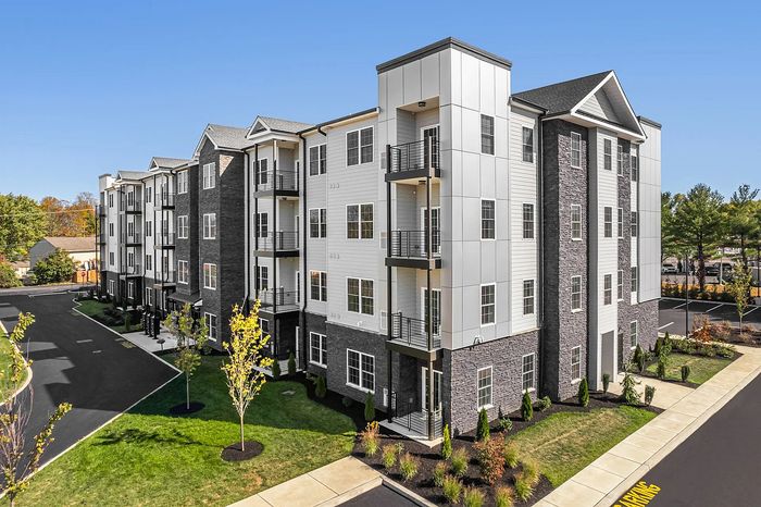 Contemporary multi-story apartment building with sleek architecture, balconies, and lush landscaping, bathed in natural sunlight.