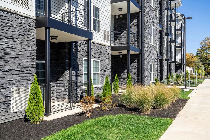 Modern apartment building with sleek stone facade and lush landscaping, showcasing a stylish blend of urban living and nature.