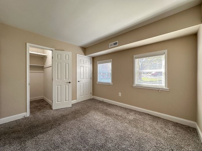Bright and inviting bedroom with plush carpet, two windows, and a spacious walk-in closet, perfect for modern living.