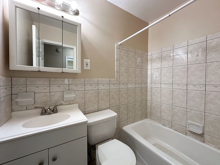 Bright and modern bathroom with elegant tiled walls, full bathtub, and sleek vanity mirror, offering a refreshing living space.