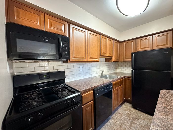 Charming kitchen with warm wooden cabinets, sleek black appliances, and a modern tiled backsplash.