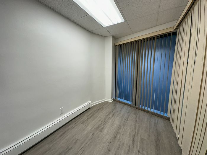 Modern room with sleek wood flooring, large vertical blinds, and bright overhead lighting, perfect for a cozy office or guest space.