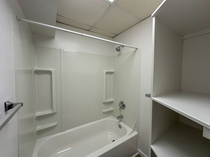 Modern bathroom with white bathtub, convenient shelving, and sleek fixtures, perfect for a stylish living space.