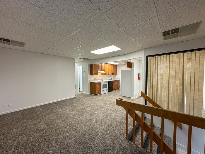 Bright and spacious apartment interior featuring an inviting open floor plan with a cozy carpeted living area, modern kitchen, and elegant staircase.