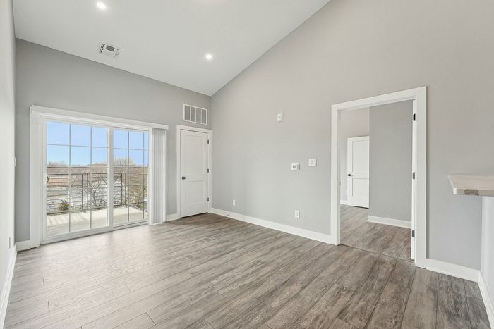 Bright and spacious living area with elegant wood flooring, large sliding glass doors opening to a scenic balcony view, and sleek modern finishes.