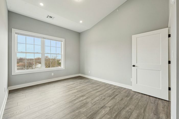 Bright and spacious room with large window, modern wood flooring, and light gray walls, creating a welcoming atmosphere.