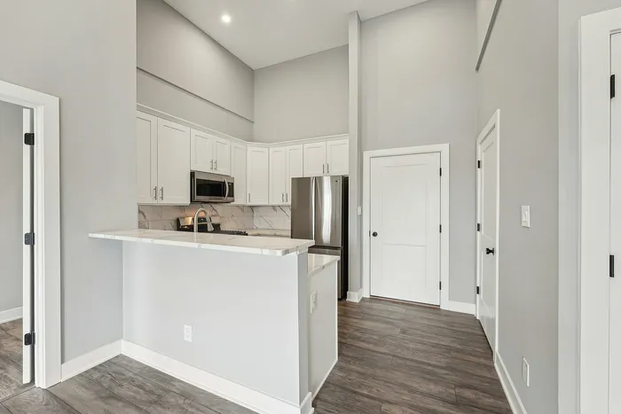 Modern kitchen with elegant white cabinetry, sleek stainless steel appliances, and a stylish marble countertop. High ceilings and recessed lighting enhance the spacious feel.