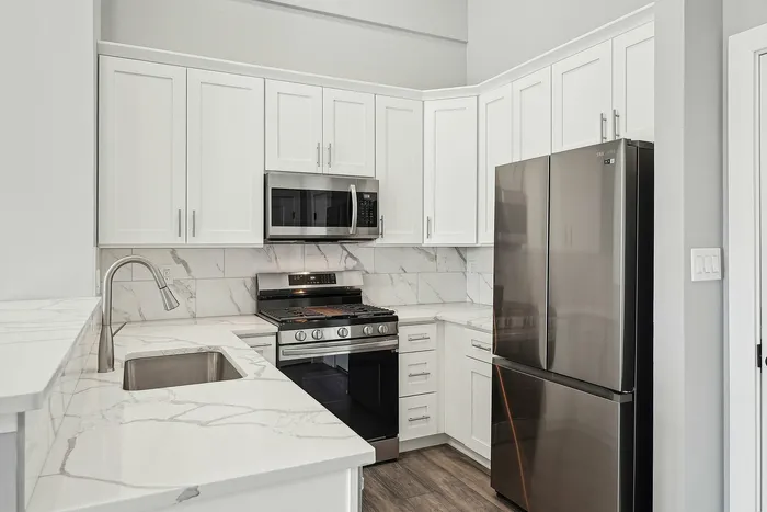 Sleek modern kitchen featuring elegant marble countertops, stainless steel appliances, and pristine white cabinetry.