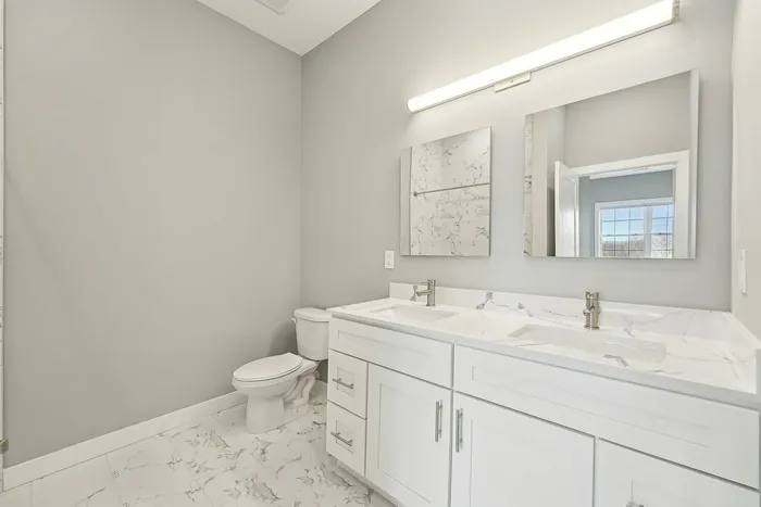 Bright and modern bathroom with double sink vanity, elegant marble countertops, and chic gray tile flooring.