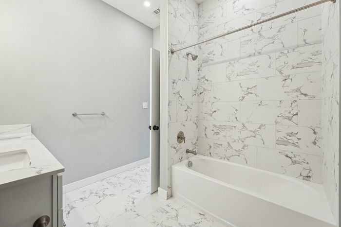 Elegant bathroom with sleek marble tile walls and flooring, featuring a luxurious bathtub and modern vanity.