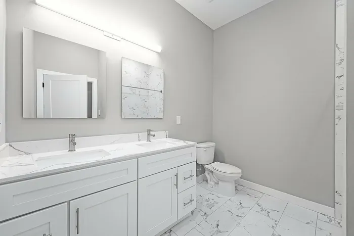 Sleek modern bathroom featuring dual sinks with elegant marble countertops and bright ambient lighting.