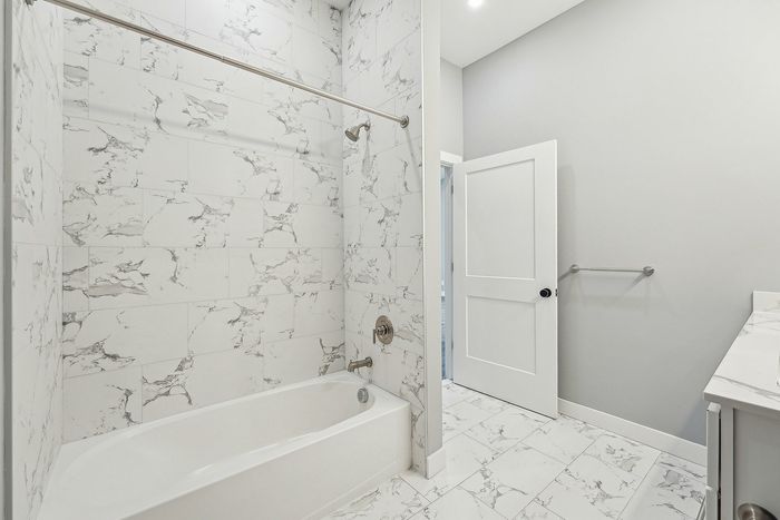 Elegant bathroom with luxurious marble tiles, pristine bathtub, and modern fixtures creating a serene spa-like ambiance.