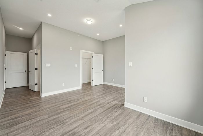 Bright and inviting empty room with elegant wood flooring and soft grey walls, featuring sleek white doors and modern lighting.
