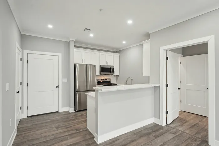 Modern kitchen with stainless steel appliances, sleek white cabinetry, and elegant hardwood floors in a contemporary apartment.