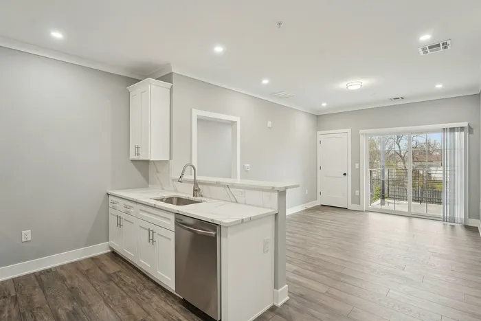 Modern open-concept apartment with sleek kitchen, elegant hardwood floors, and bright sliding glass doors leading to a balcony.