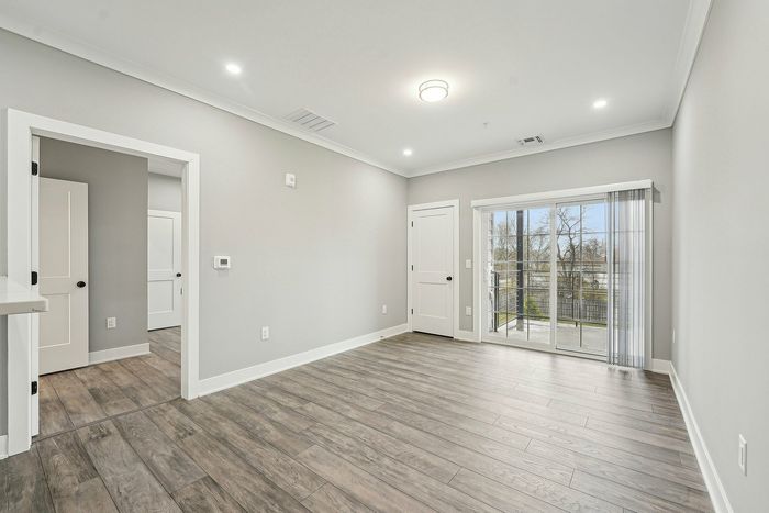 Bright and modern living area with sleek wood flooring, sliding glass door leading to a balcony with serene outdoor views.