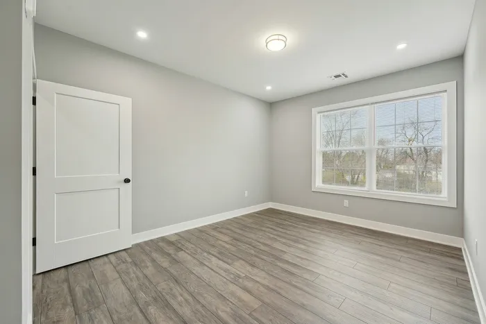 Bright, spacious room with sleek wood flooring and large window offering abundant natural light.
