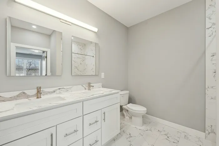 Modern bathroom with dual sinks, large mirrors, and elegant marble accents.