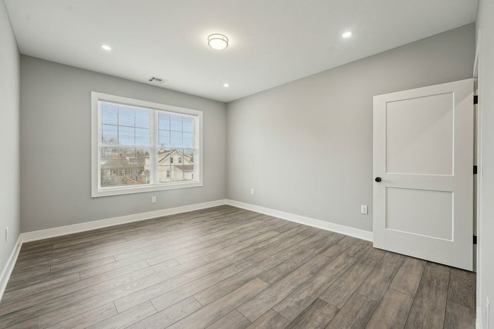Bright and airy room with elegant wood flooring, offering ample natural light through large windows for a serene living space.