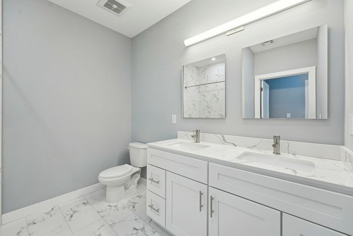 Elegant bathroom featuring a modern double vanity with sleek white cabinets and polished marble countertops, complemented by a chic gray wall and stylish floor tiles.