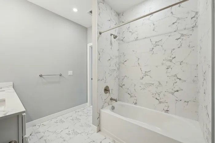 Modern bathroom with elegant marble tile design, featuring a bathtub-shower combination and sleek gray walls, creating a serene and luxurious atmosphere.