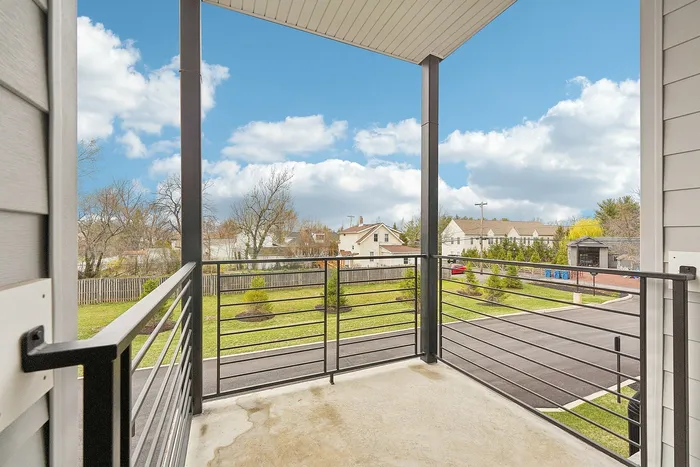 Charming apartment balcony with a picturesque view of a serene neighborhood and lush green yard under a clear blue sky.