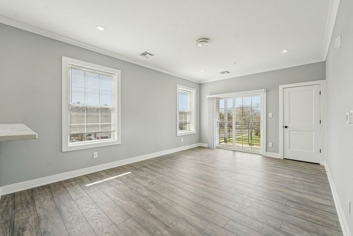 Bright and airy living space with sleek hardwood floors, large windows, and a door leading to a private balcony, ideal for relaxation.