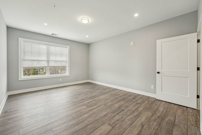 Bright and spacious room with elegant hardwood flooring, large window bringing in natural light, and modern recessed lighting.