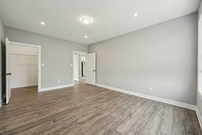Spacious empty room with elegant wood floors, soft gray walls, recessed lighting, and a walk-in closet.