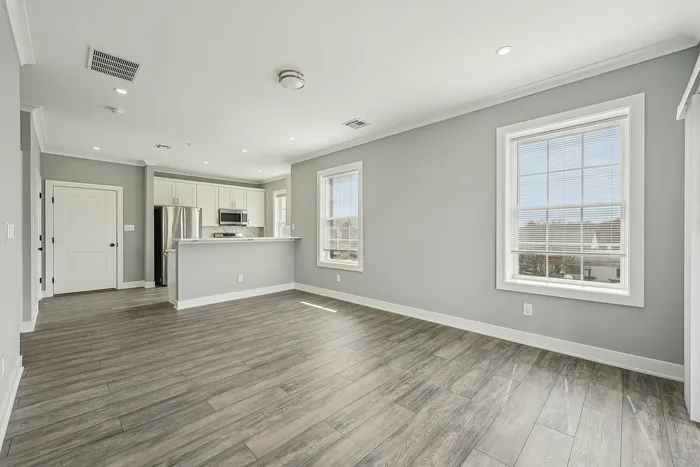 Bright modern apartment with open-plan layout, featuring sleek hardwood floors, large windows providing natural light, and a contemporary kitchen.