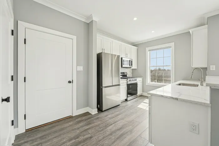 Bright, modern kitchen with stainless steel appliances, elegant marble countertops, and large window for natural light.