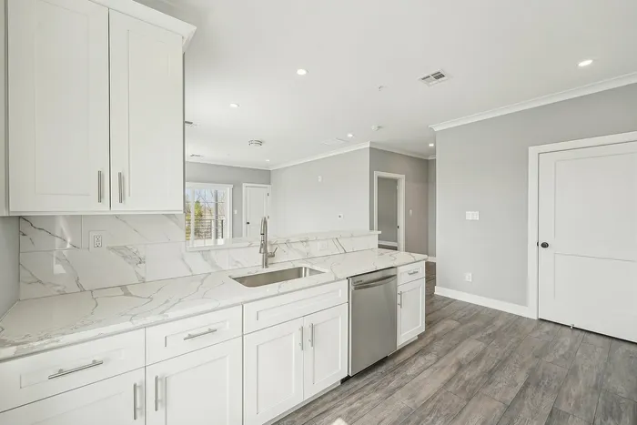 Luxurious modern kitchen with sleek white cabinets, elegant marble countertops, and stainless steel appliances, flowing into a bright and airy open-concept living space.
