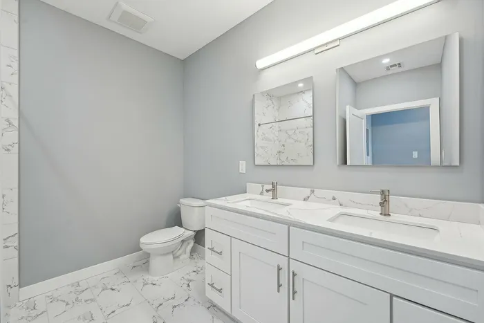 Elegant bathroom with dual sinks, sleek modern faucets, and stylish marble countertops, complemented by soft gray walls and chic tile flooring.