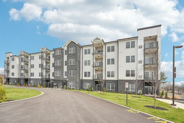 Contemporary apartment building with elegant exterior, spacious balconies, and lush green landscaping under a bright blue sky.