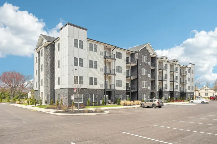 Modern 4-story apartment building with elegant stone and siding finish, featuring spacious balconies and ample parking, under a bright blue sky.