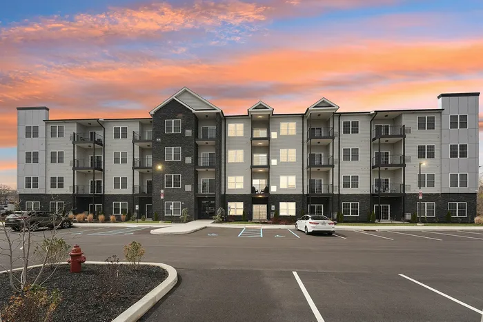 Modern apartment building with balconies and ample parking, set against a vibrant sunset sky.