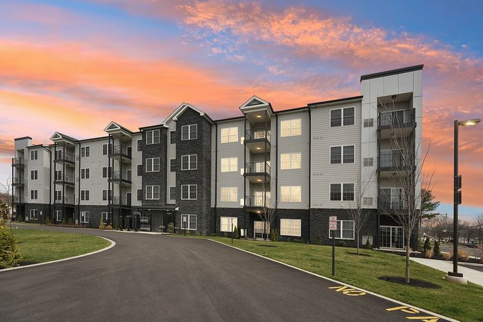 Elegant apartment building with modern architecture against a stunning sunset sky, showcasing serene green lawns and well-lit walkways.