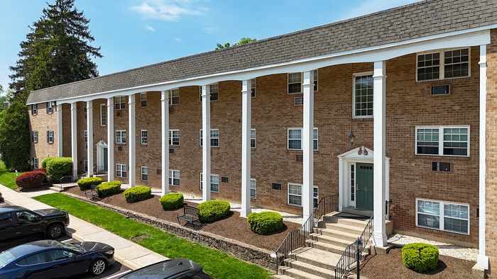 Charming brick apartment building with classic white pillars and lush landscaping, offering a welcoming entrance.
