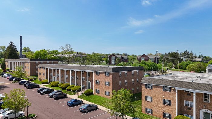 Charming brick apartment complex with classic columns and ample parking, surrounded by lush greenery and a clear blue sky.