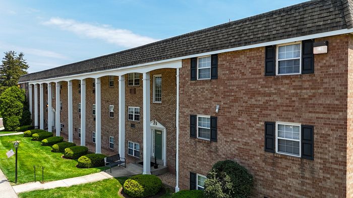 Charming brick apartment building with classic white columns, lush greenery, and inviting entrance path.
