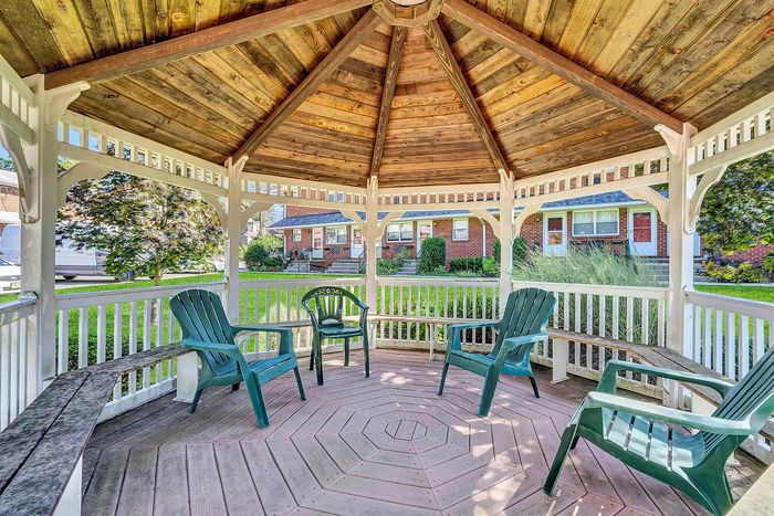 Charming wooden gazebo with inviting seating, offering a peaceful retreat in a lush green neighborhood.